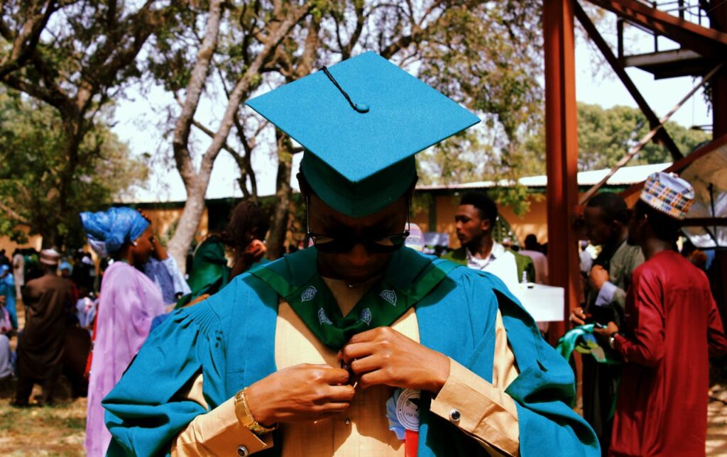 Graduate adjusting gown during an outdoor ceremony, vibrant and celebratory atmosphere.